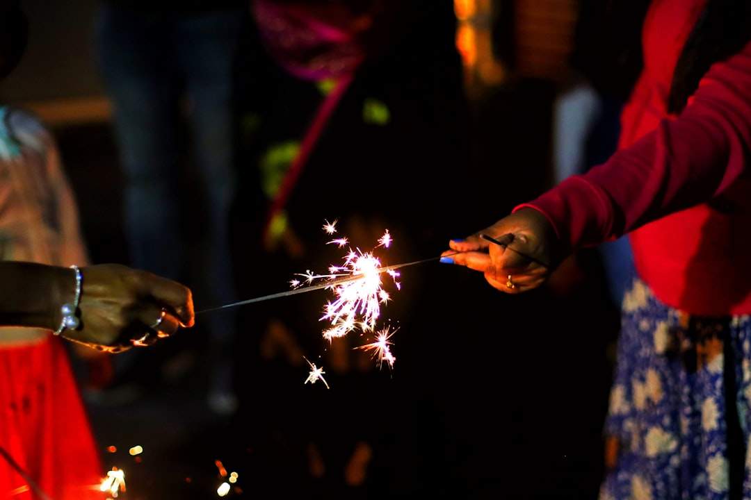 Eine Nahaufnahme einer Hand, die eine Wunderkerze hält, mit Bokeh-Lichtern im Hintergrund, die eine festliche und feierliche Atmosphäre schaffen, perfekt für eine Neujahrsunterschrift.