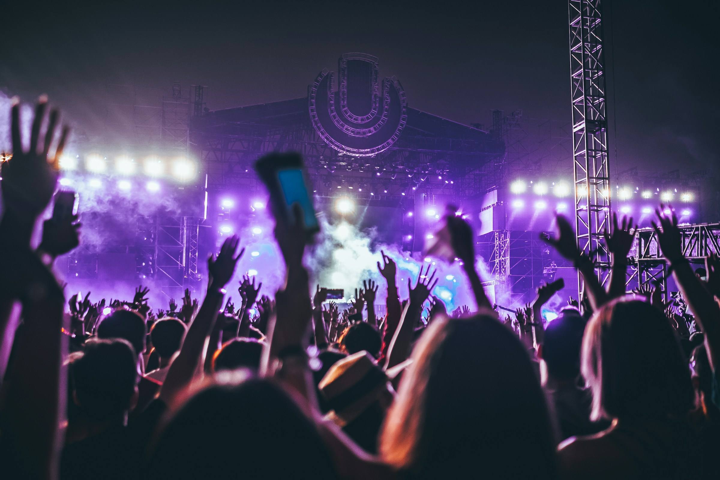 Une photo vibrante d'une foule nombreuse et excitée au festival de musique Les Ardentes avec les lumières de la scène en arrière-plan.