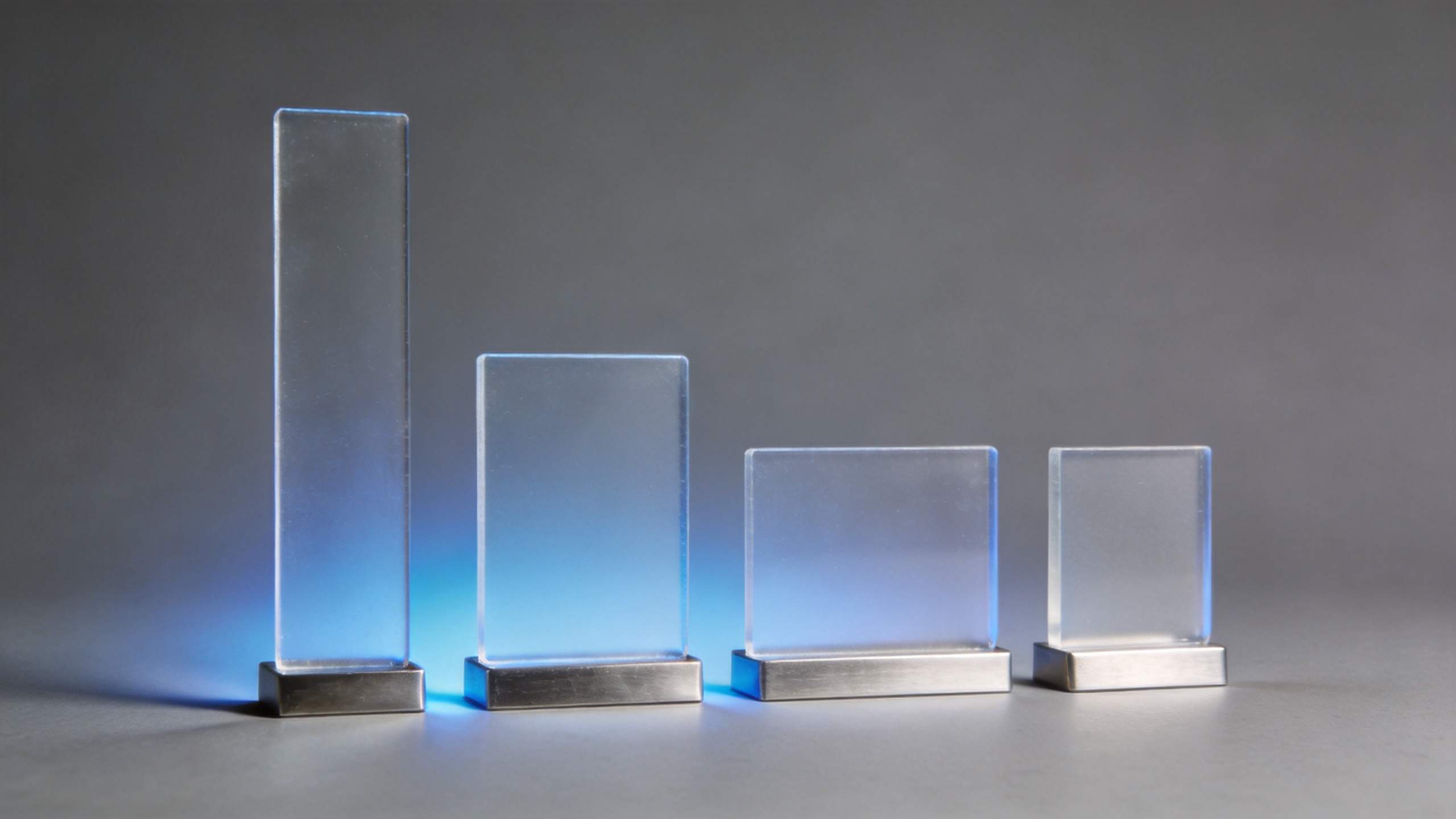 Four transparent rectangular award plaques on silver bases, with the tallest one at left