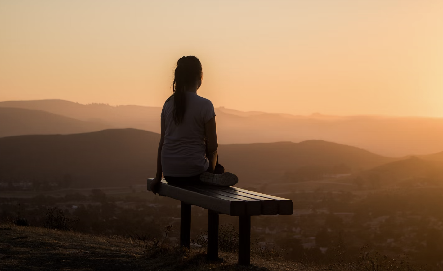 A person standing on a mountain peak looking at a vast landscape, representing deep thought and contemplation.