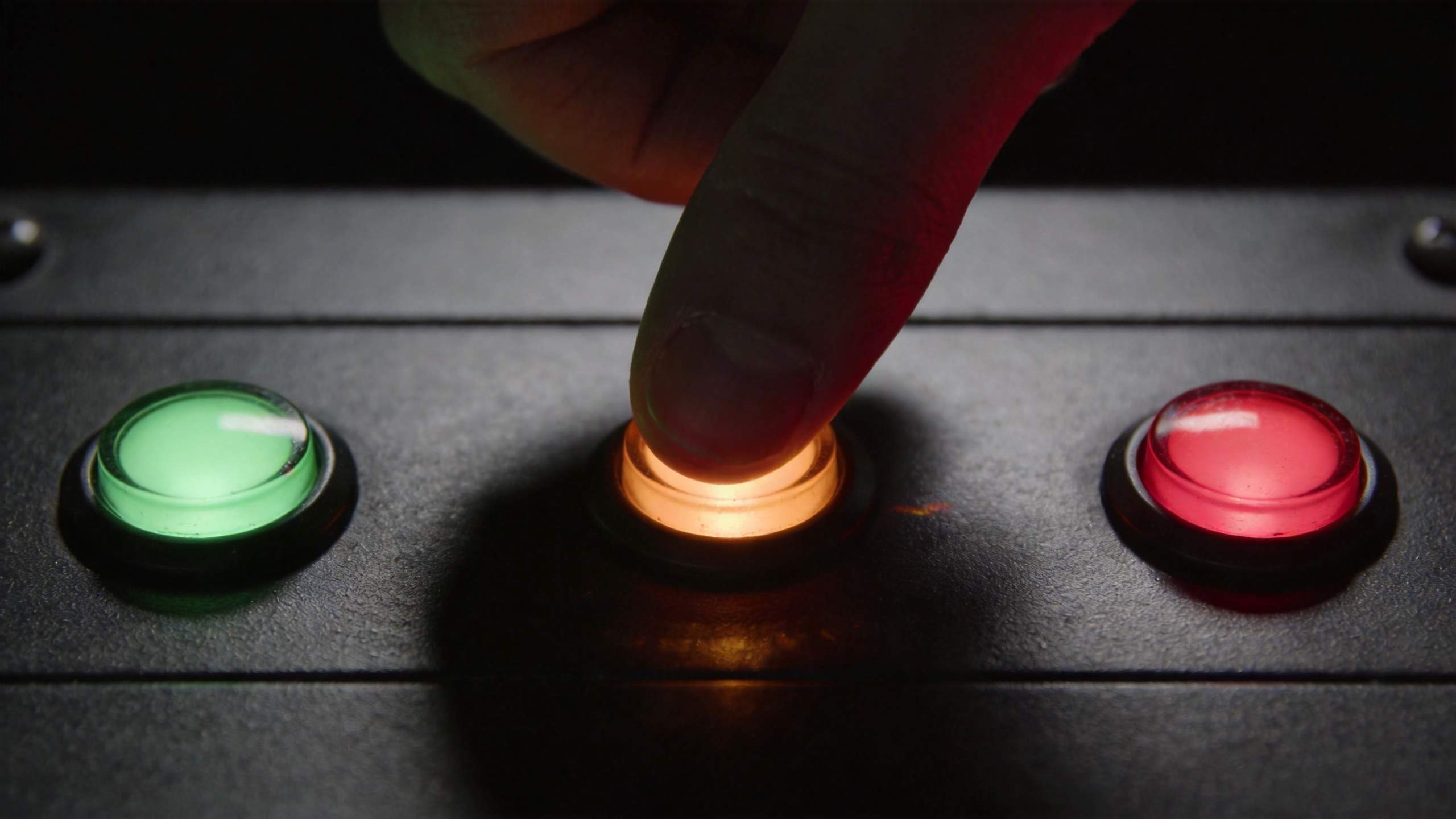 Finger pressing a glowing orange button beside green and red buttons