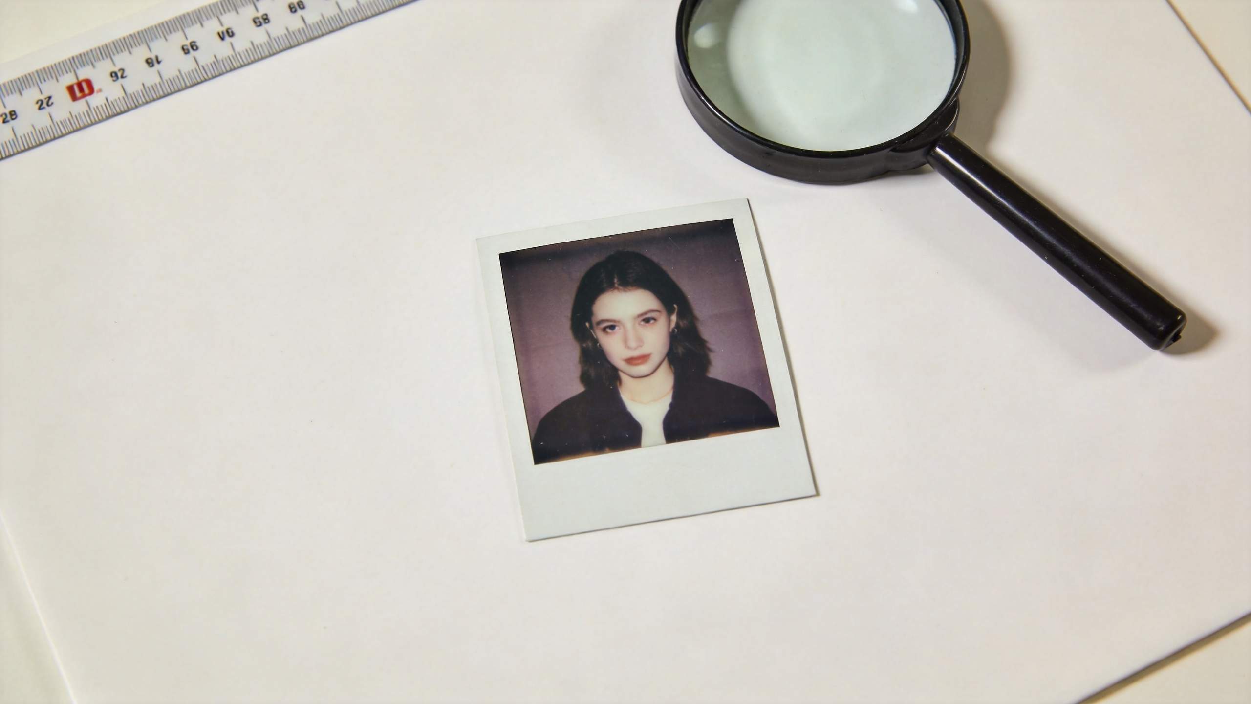 Polaroid portrait on a white desk with a magnifying glass and ruler