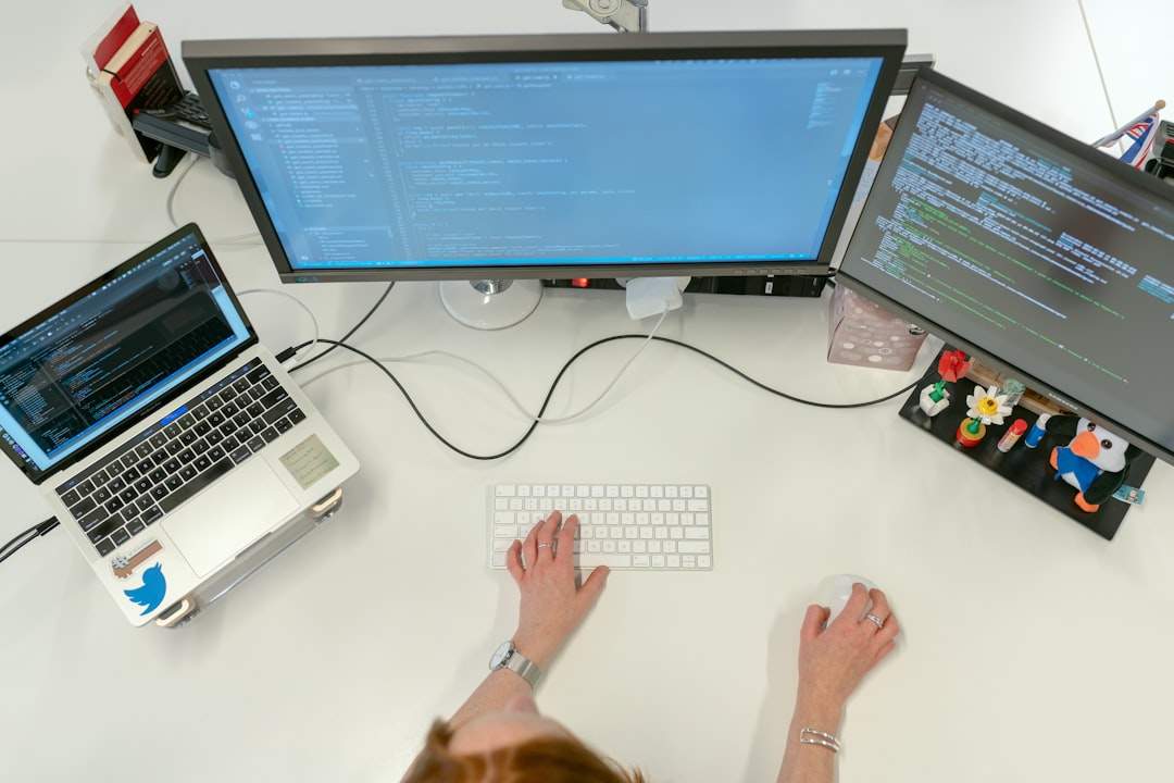 A person sitting at a desk, comparing two different AI software interfaces on their computer monitors