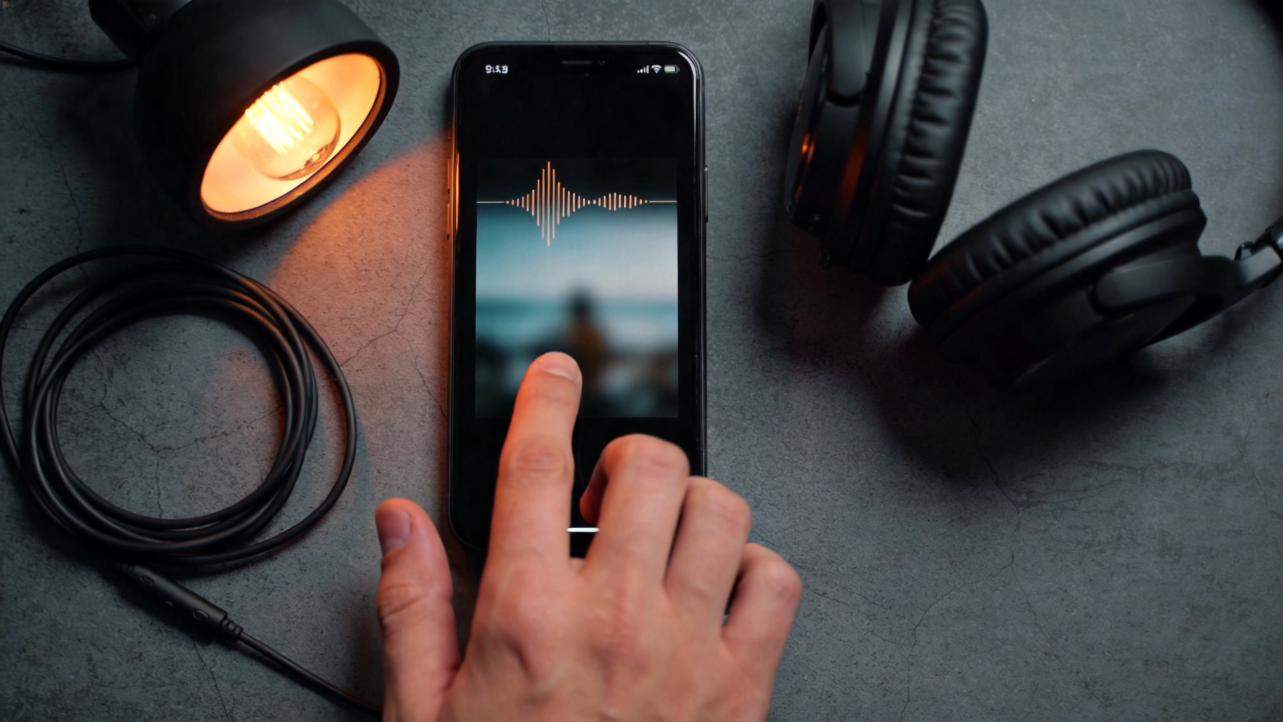 Hand tapping a smartphone beside headphones and a warm studio light