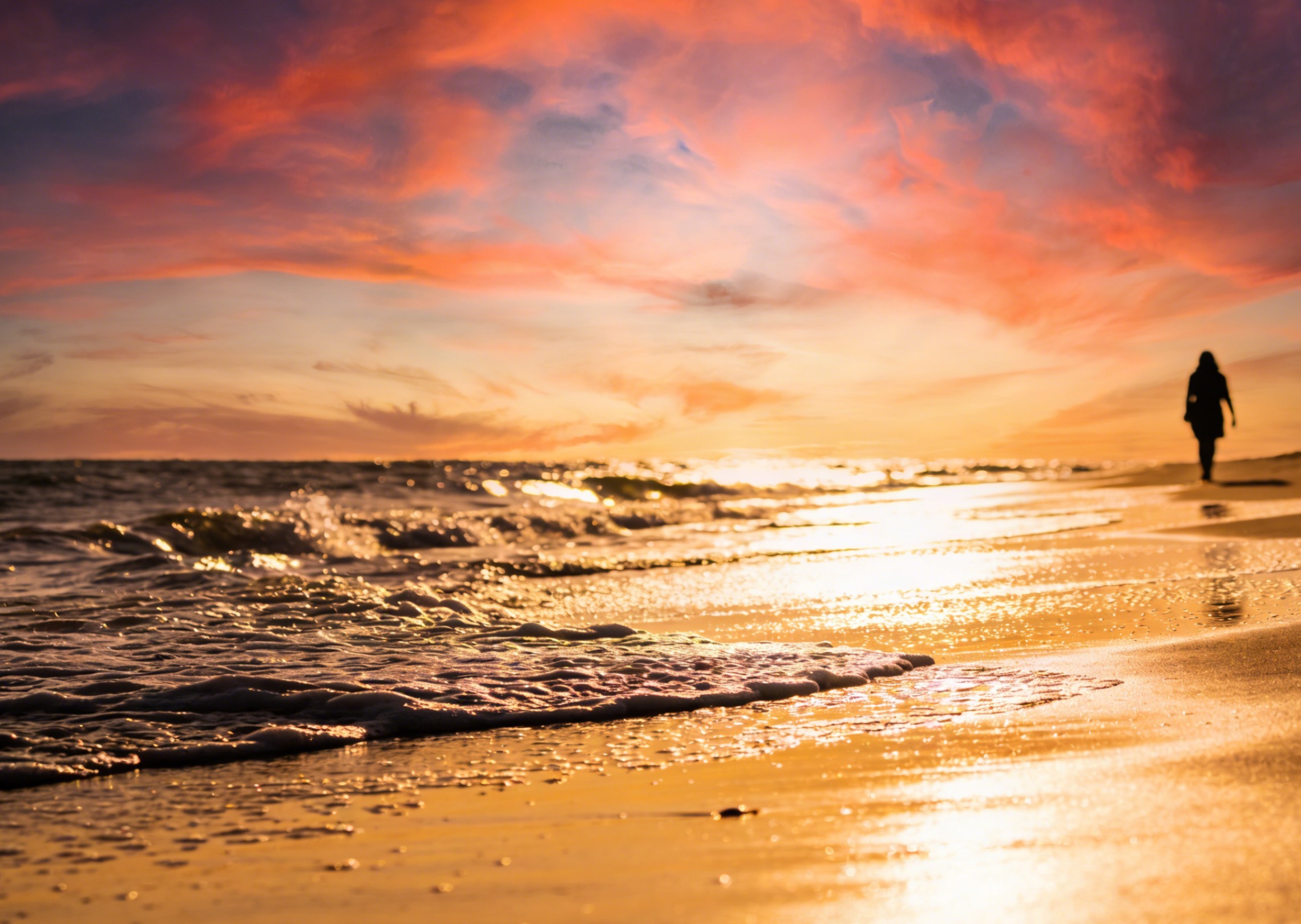 Generate a video of a beach at sunset with waves gently rolling and a person walking along the shore