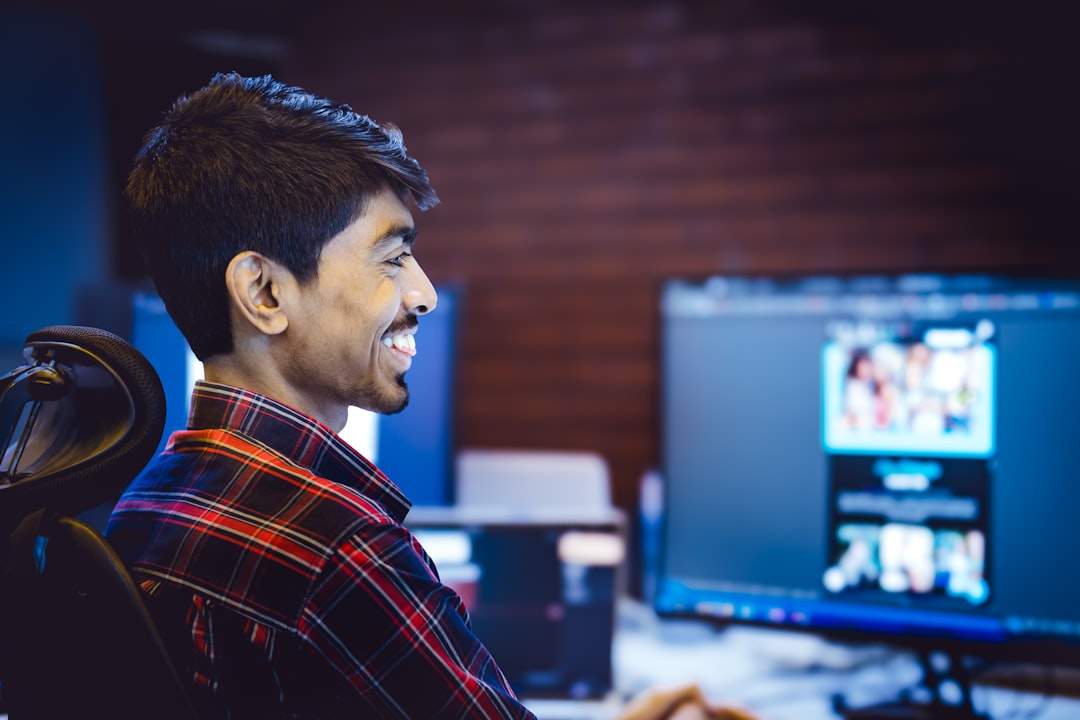 Seseorang tersenyum saat mengedit video di laptop, dengan elemen grafis mengambang di layar