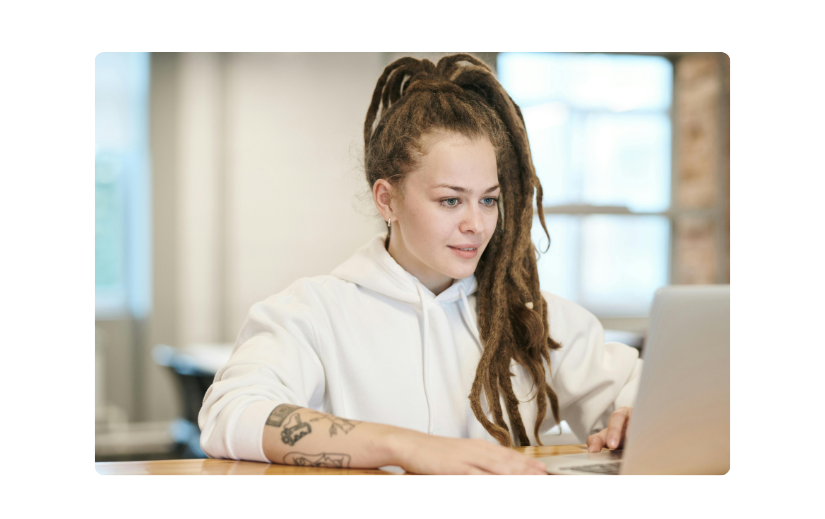Junge Frau in einem weißen Hoodie arbeitet an einem Laptop und erkundet kreative Einkommensideen in einem modernen Coworking-Space.
