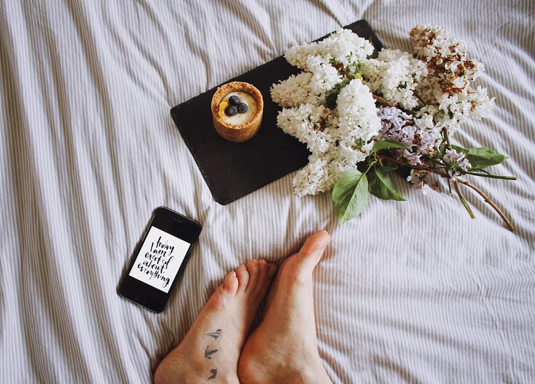 Imej berbaring rata dengan telefon pintar yang menunjukkan siaran Instagram, cawan kopi dan bunga kecil.