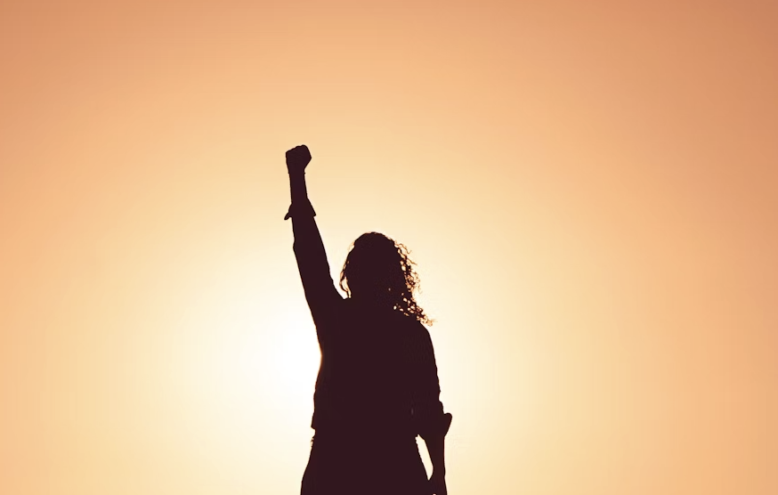An inspiring image of a woman looking confidently at the camera, with a soft, warm background that conveys empowerment and positivity. The woman should represent a modern, relatable figure.