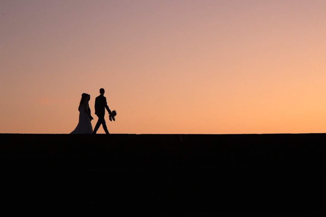 Un'immagine romantica di una coppia che si tiene per mano mentre cammina verso un tramonto.