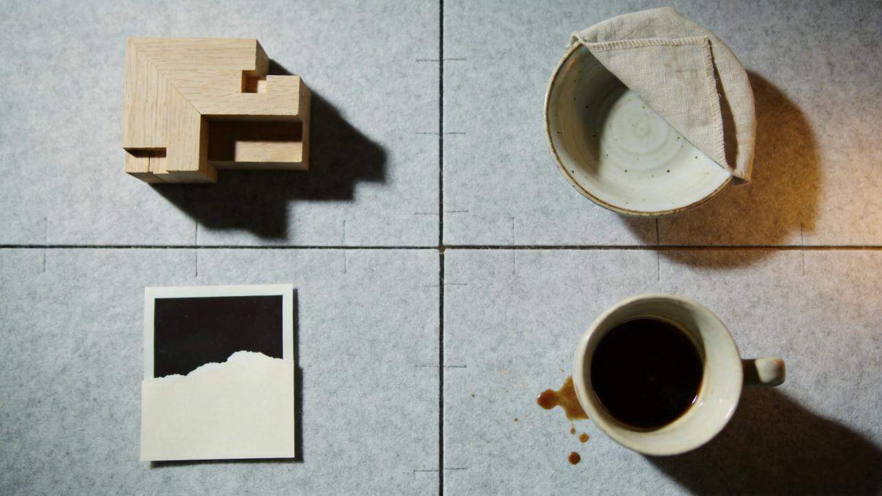 Top-down view of four objects on a tiled surface: wooden blocks, a covered bowl, a Polaroid photo, and a cup of coffee