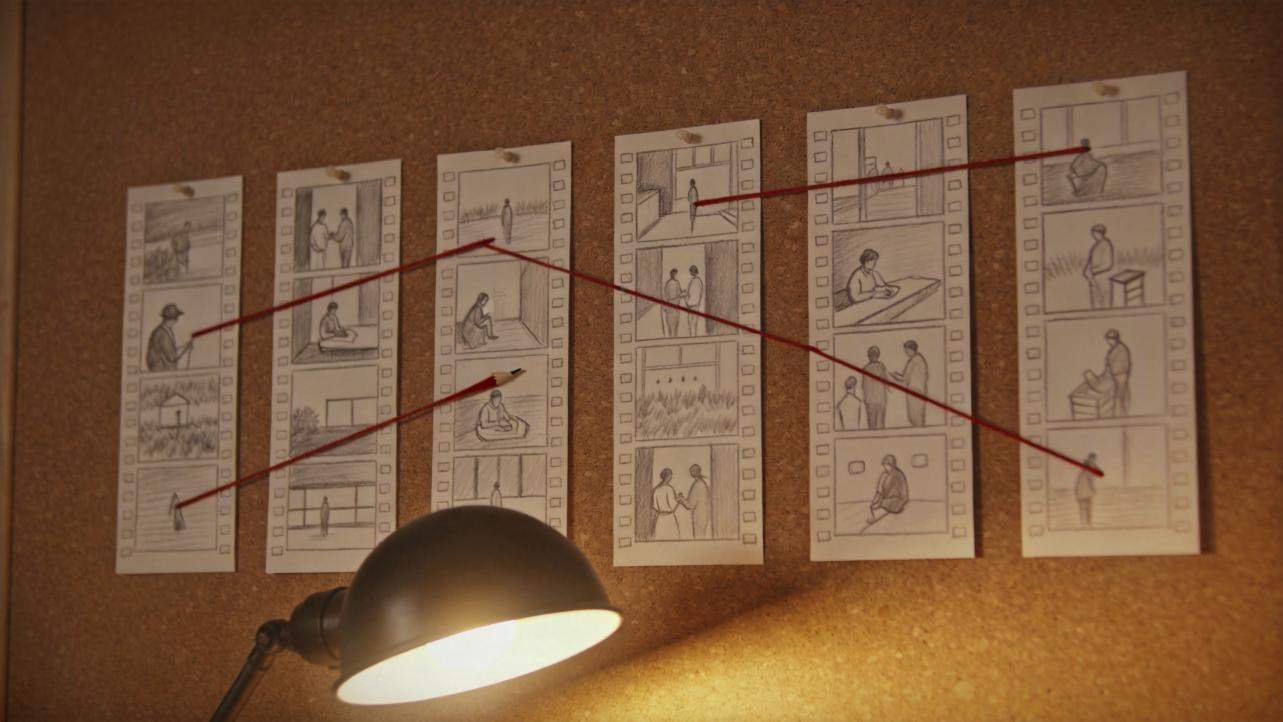 Storyboard sketches pinned to a corkboard, linked by red strings above a desk lamp.