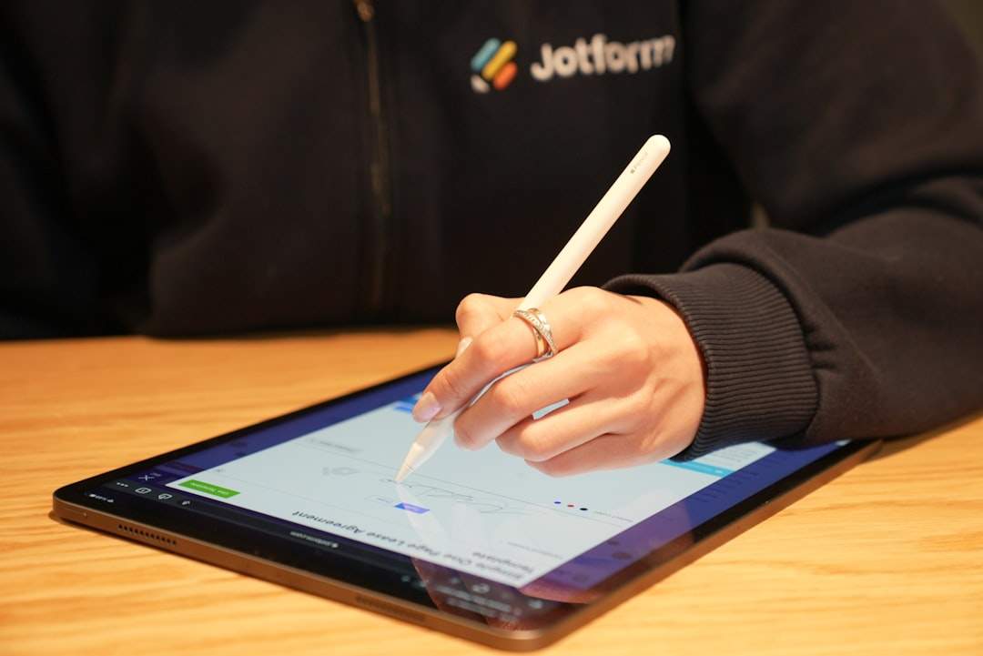 A person writing in a notebook with a laptop in the background