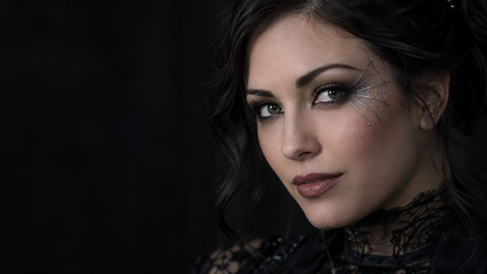 Silver Web Eyeliner: A fictional adult woman's close-up face with delicate silver spiderweb eyeliner radiating precisely from one outer eye corner, black lashes and clean natural skin.