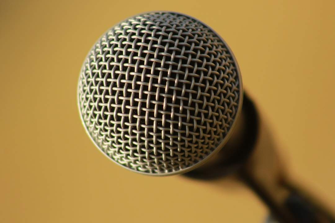 Isang taong nagsasalita sa mikropono na may mga sound wave na nagmumula sa kanilang bibig, na kumakatawan sa voice synthesis.
