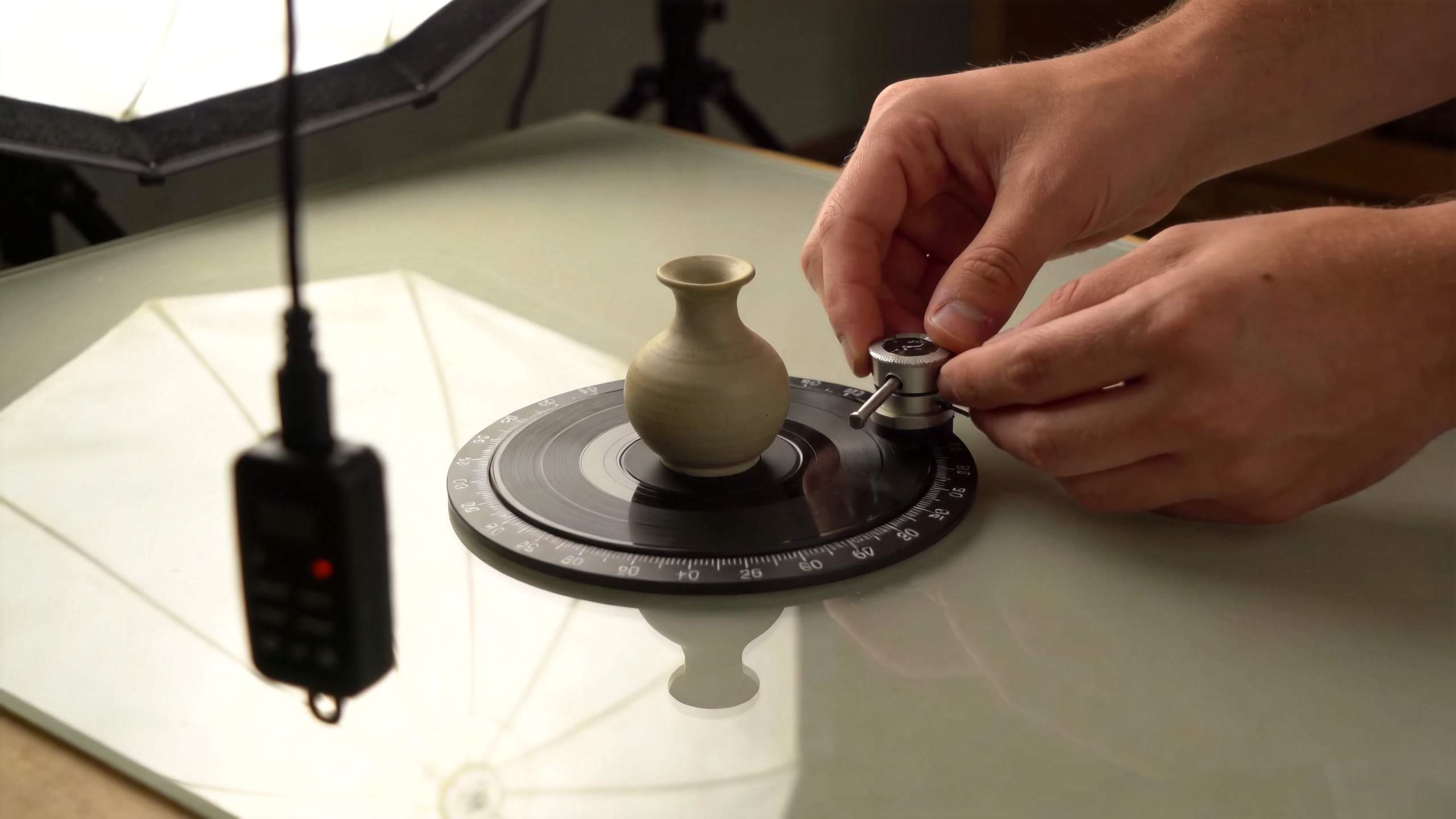 Hands adjust a small vase on a rotating turntable under studio lights