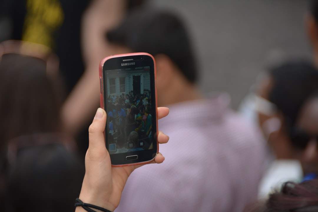 A person's hand holding a smartphone displaying a photo that has been beautifully edited with filters, with a laptop showing CapCut's interface in the background.