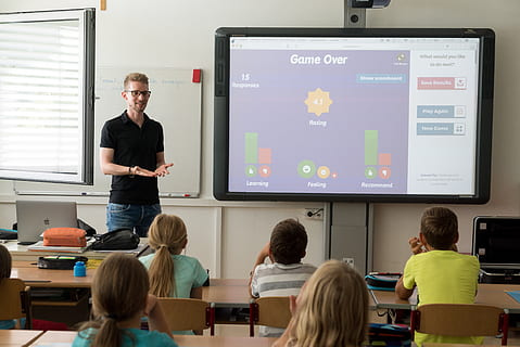 Teacher interacting with students in classroom with books and boards