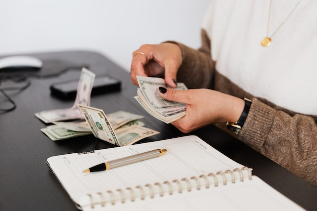 Persona contando billetes en un escritorio con un cuaderno, simbolizando ideas de ingresos pasivos y oportunidades de ganancias en línea.