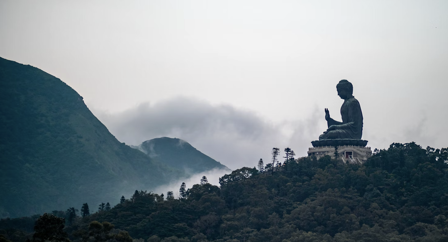 A serene Buddha statue in a peaceful garden setting, with a soft, out-of-focus background. The statue is the main focus, exuding a sense of calm and tranquility.