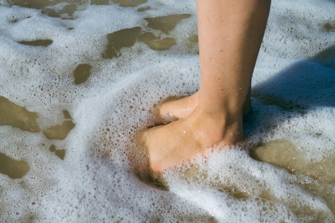 Close-up of a person's feet in the sand with gentle waves washing over them.
