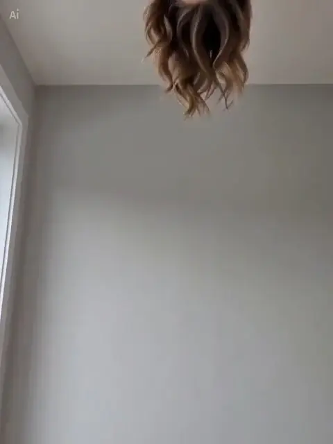Wavy hair hanging upside down from the top edge against a plain gray wall