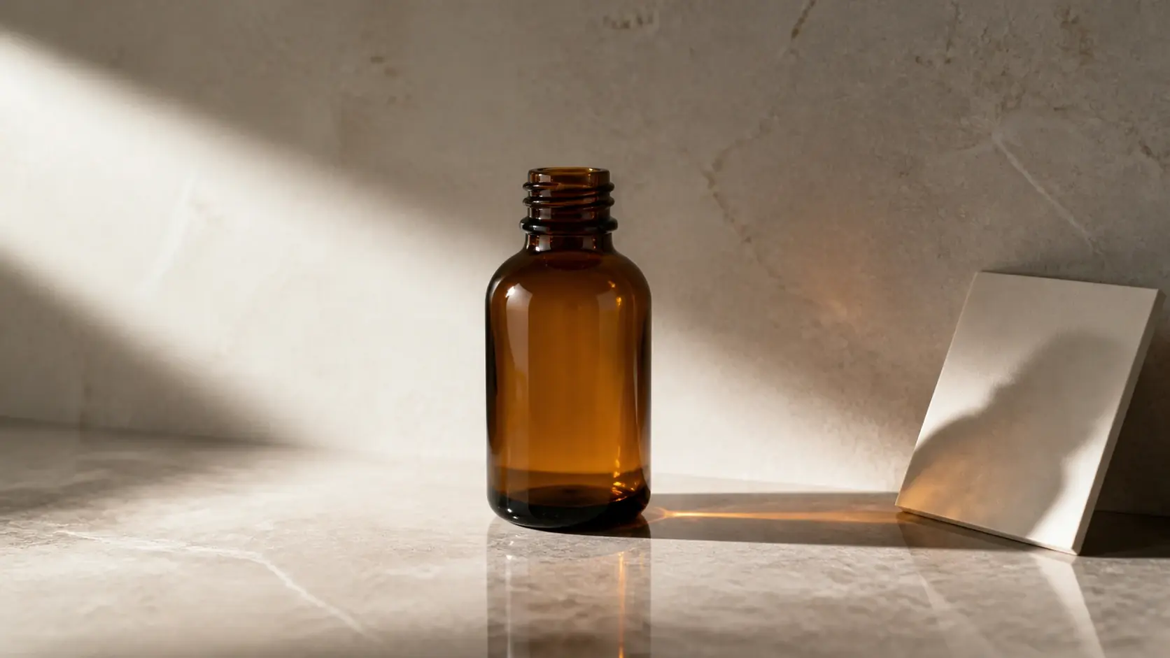 Amber glass bottle on a marble surface beside a white card in diagonal sunlight