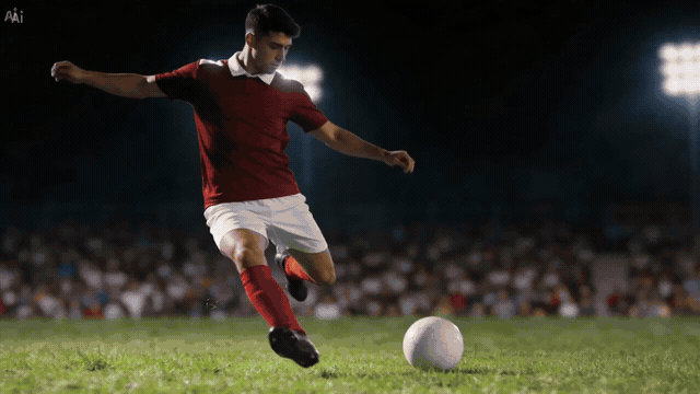 Soccer player in red jersey kicking a ball on a lit stadium field