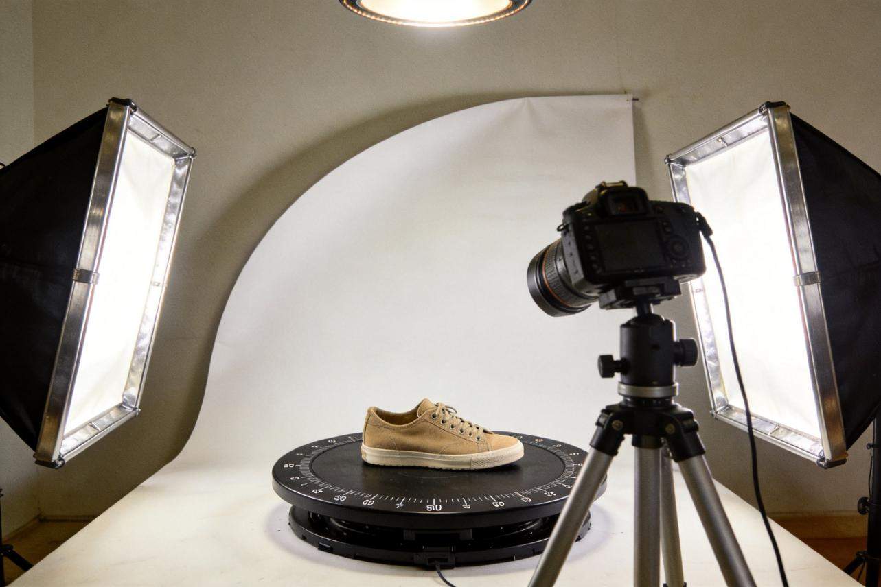 Camera on tripod photographing a shoe on a rotating turntable with studio lights on both sides