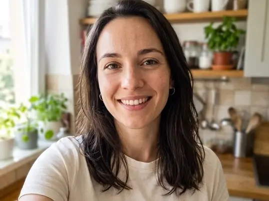 Smiling woman taking a selfie in a bright kitchen with shelves and plants behind her