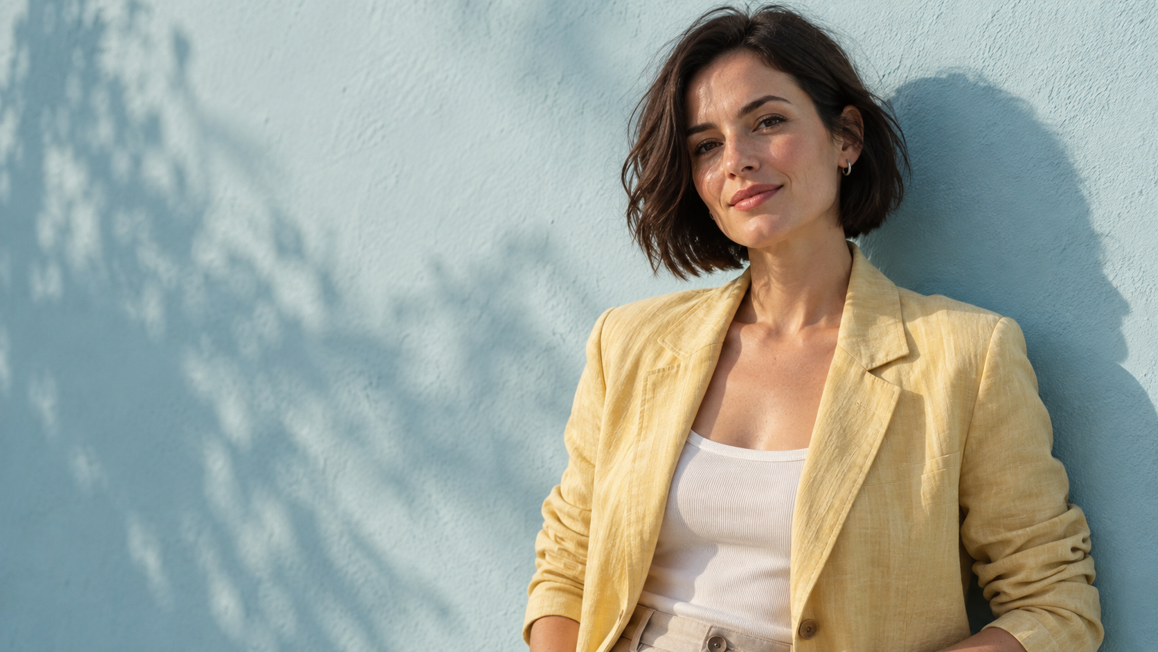 Concept portrait of an adult woman in a butter-yellow jacket beside a sunlit cyan wall