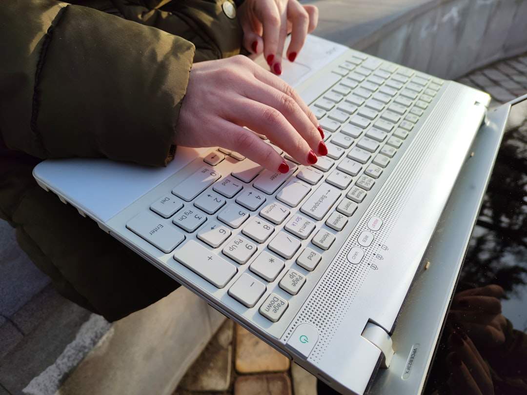 A close-up of a person's hands typing on a laptop, with a blurred background of a library.