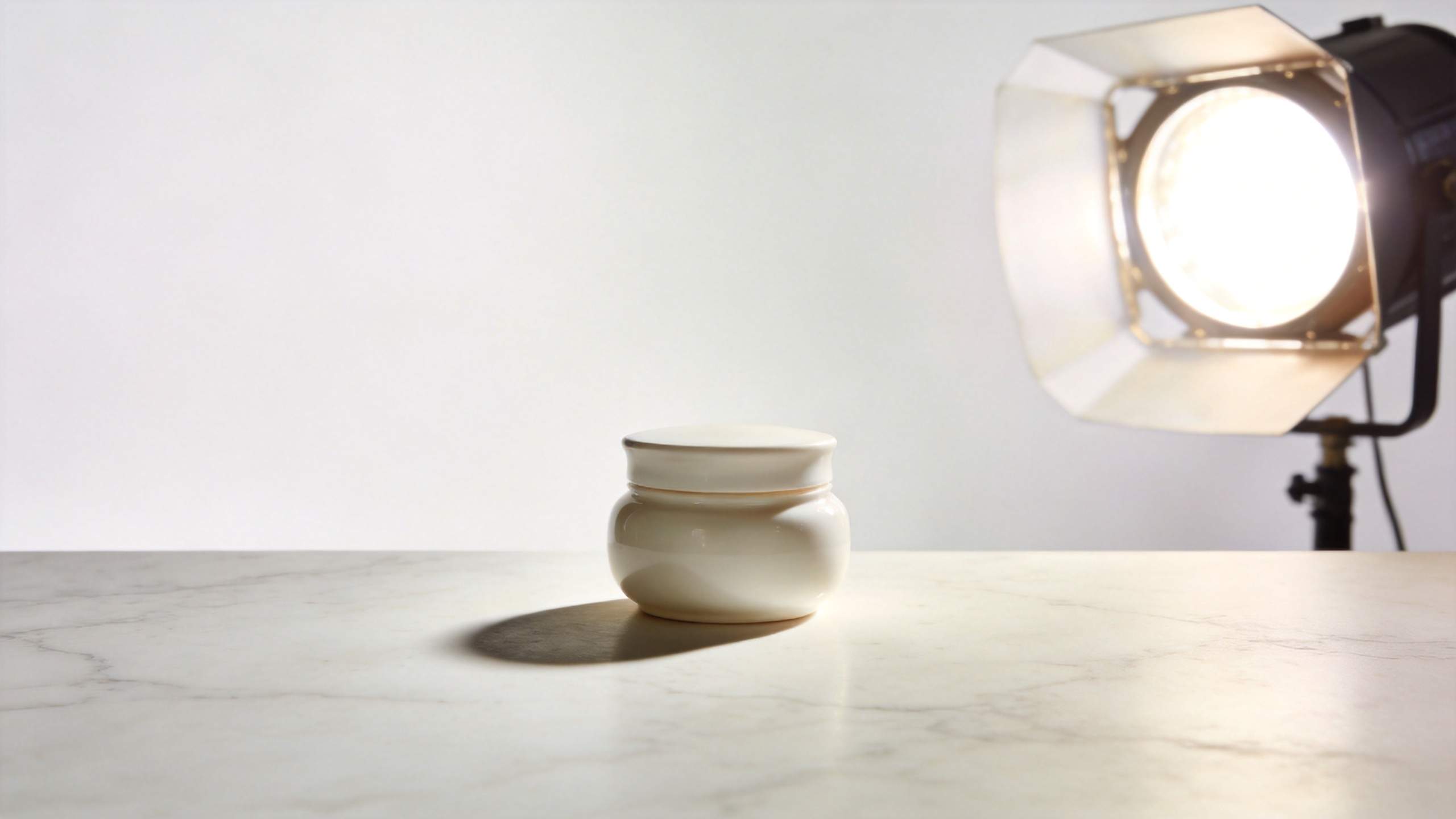 Cream cosmetic jar on marble surface beside a bright studio light