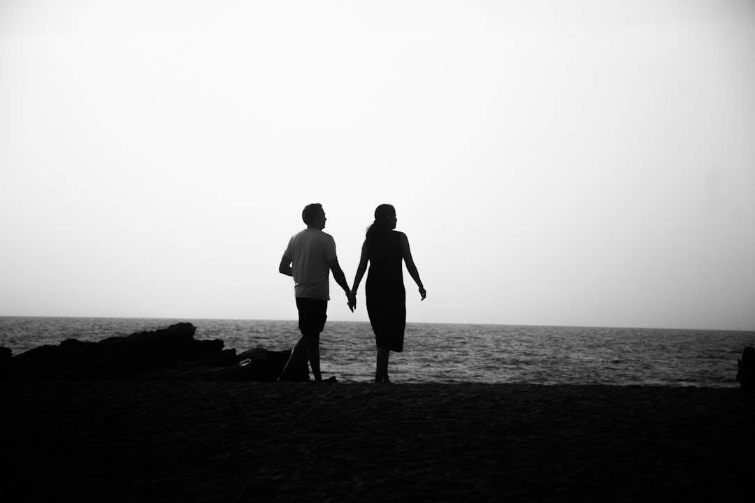 A silhouette of a couple holding hands and walking on the beach at sunset.