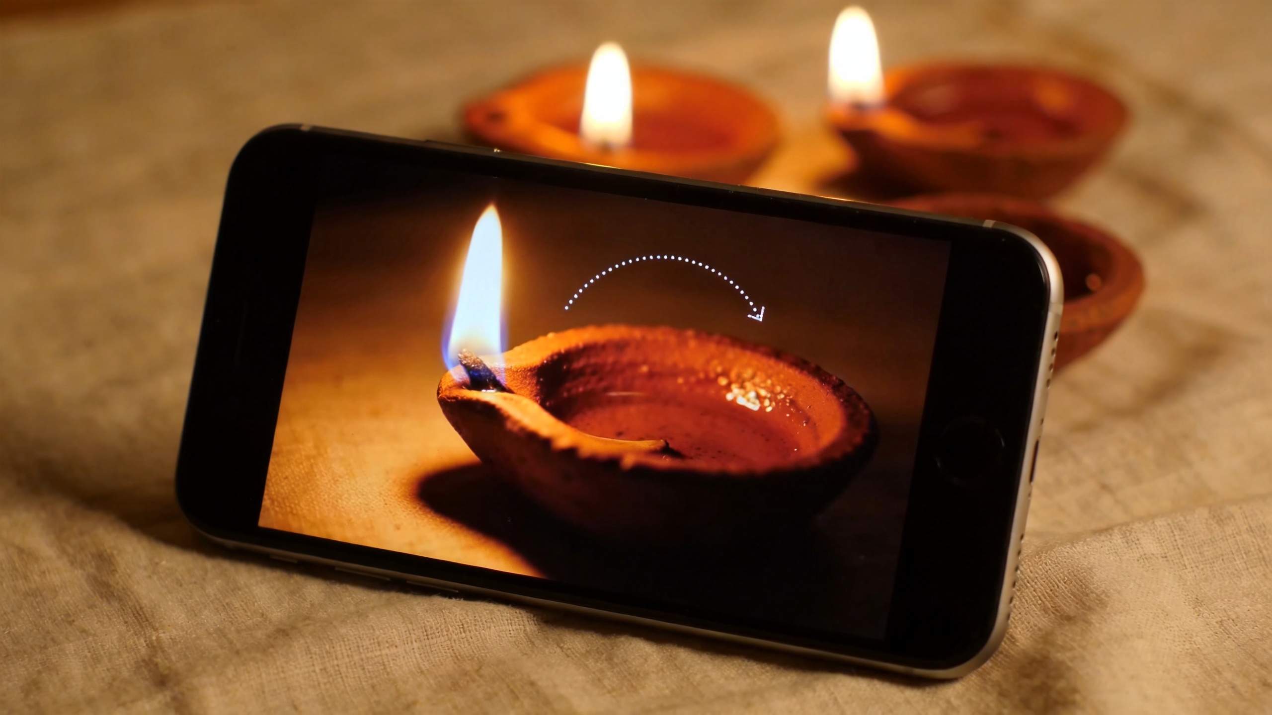 Phone displaying a lit diya with a dotted curved arrow above it